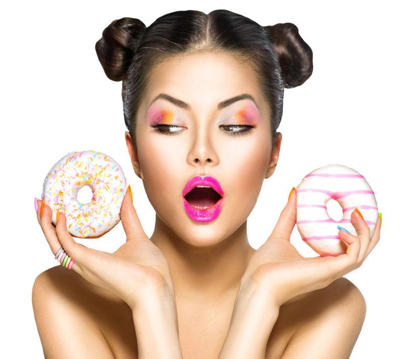 画着精致妆容的美女手里拿着两个甜甜圈
