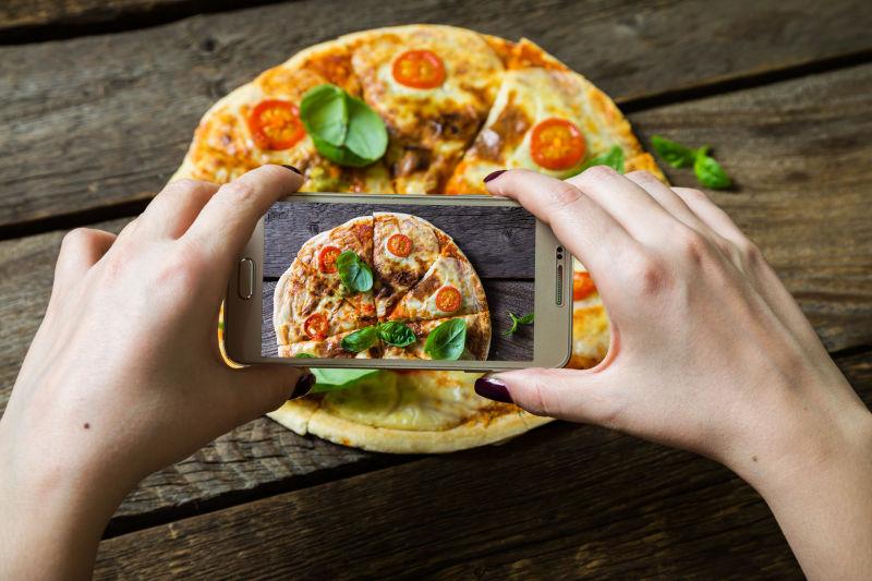 女人拿着手机拍比萨饼