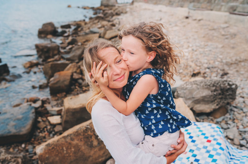海滩岩石边的女儿抱着亲吻妈妈的脸颊