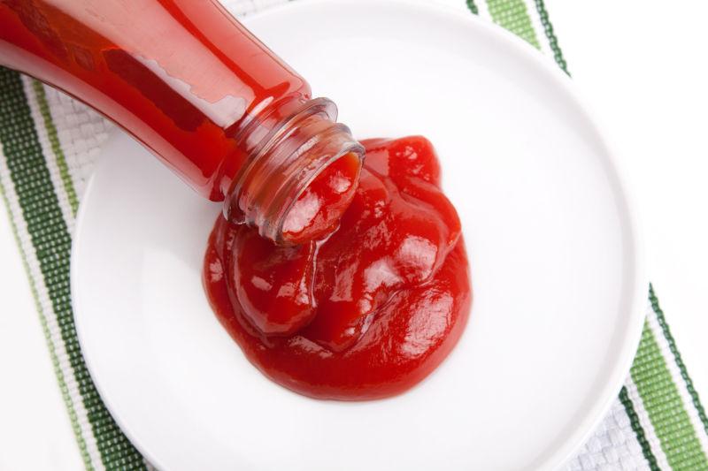 从瓶子里倒到白色盘子中的番茄酱