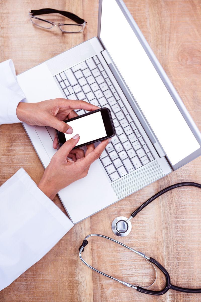 在办公桌上用智能手机笔记本的医生