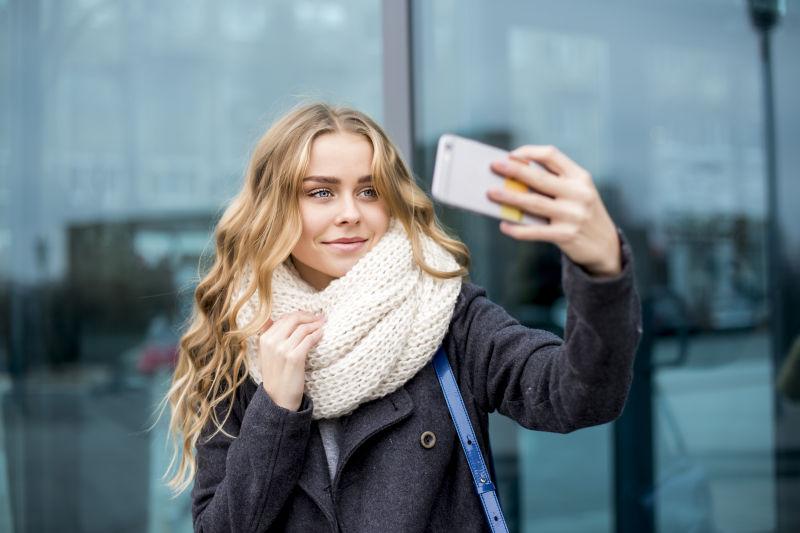 窗户边使用手机自拍的金发美女