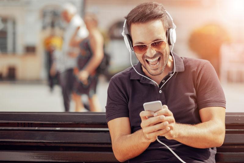 在户外玩手机戴耳机大笑的男人