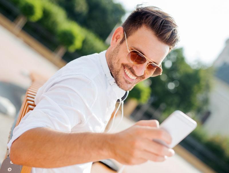 在户外拿着手机微笑的年轻男人