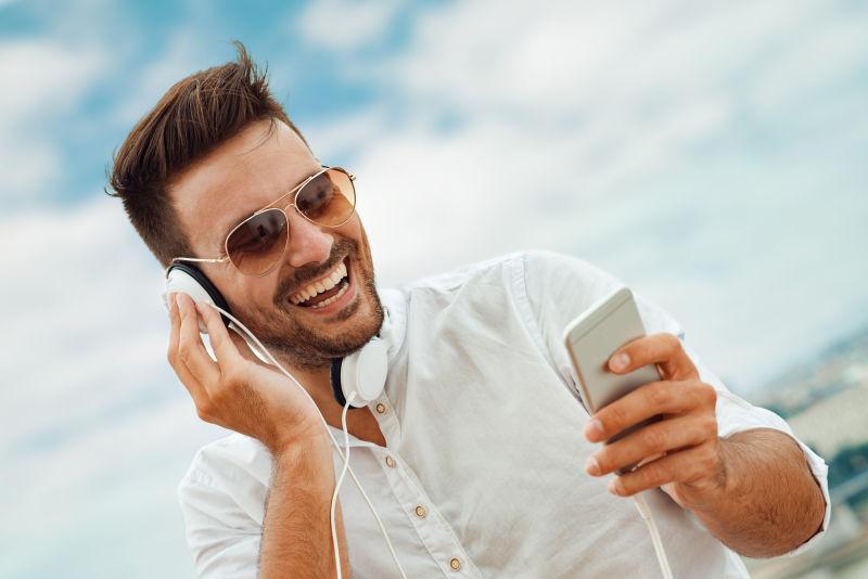 大笑的男人戴耳机玩手机