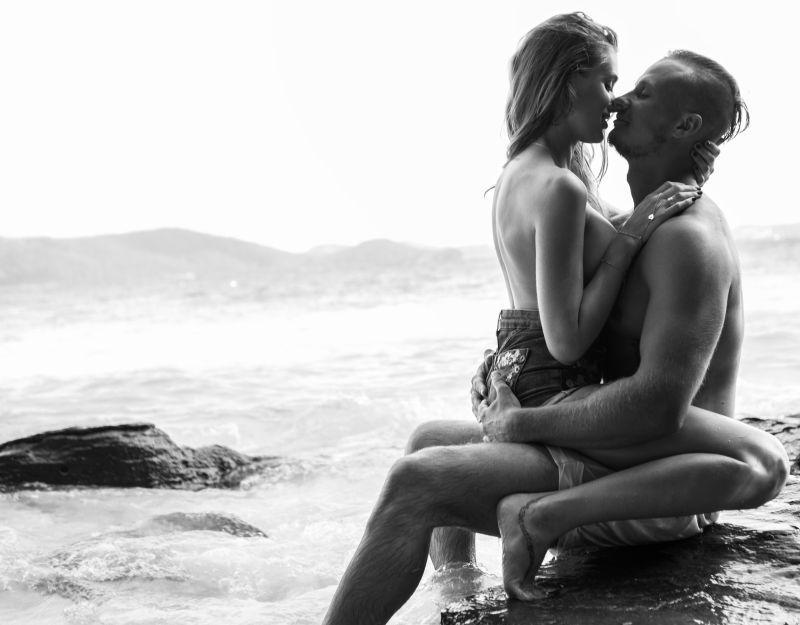 年轻男女坐在海边岩石上热吻