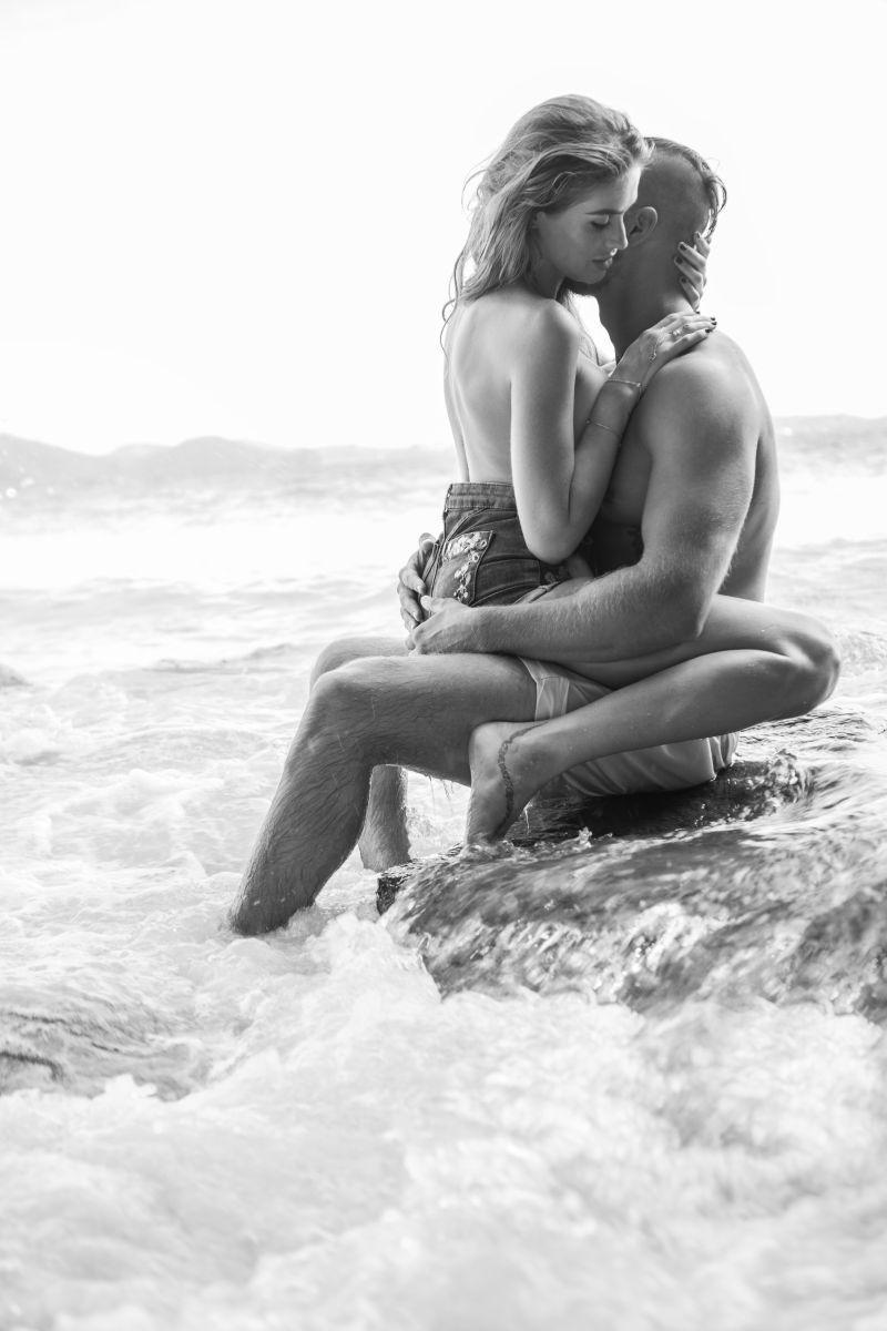 迷人的年轻情侣偶拥抱在海边的岩石上
