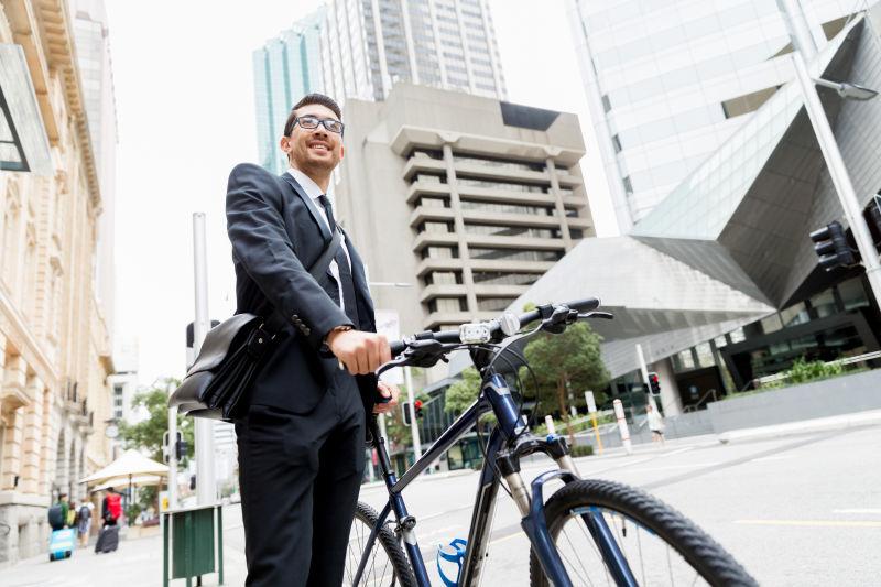 城市建筑背景下推着自行车的年轻商人