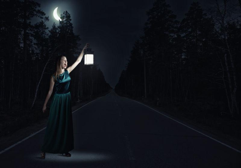 年轻的漂亮女人穿着绿色长裙提着灯笼站在黑暗的路上
