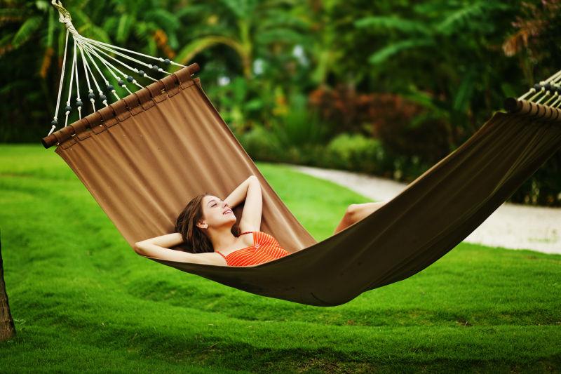 户外绿色草坪吊床上的年轻美女