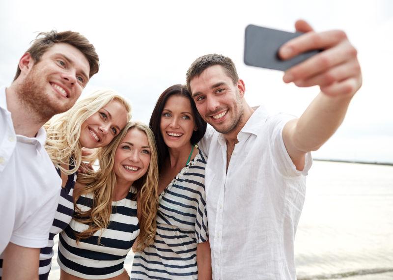 沙滩上使用智能手机自拍的微笑的好友