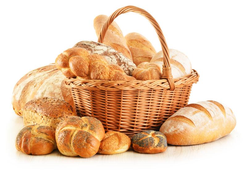 白色背景上装满面包的竹篮和竹篮边不同形状的小麦面包
