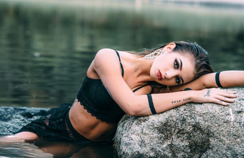 清澈的水边头枕着胳膊侧躺在石头上的黑衣美女