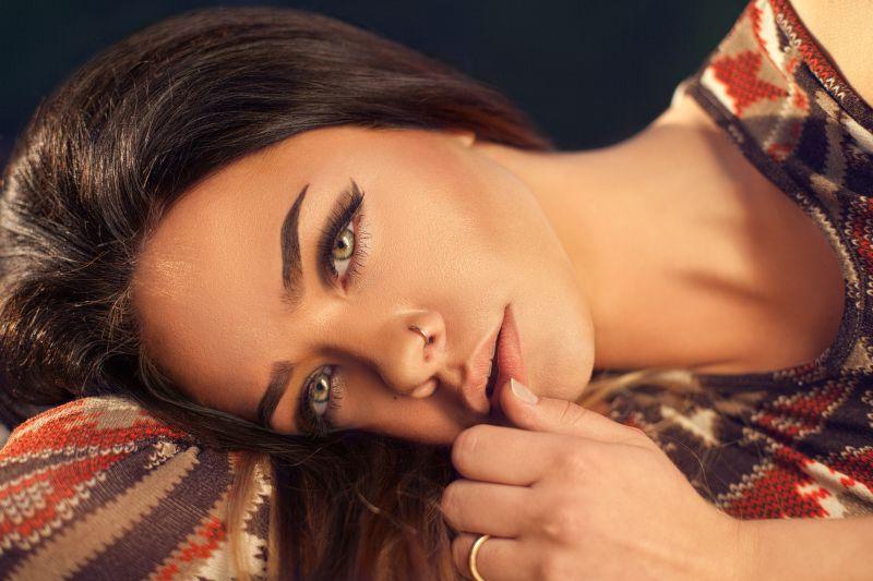 黑色背景上头枕着胳膊侧躺的有着精致妆容的美女