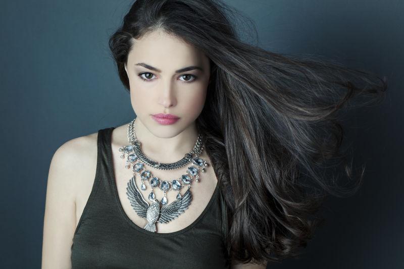 灰色背景下的戴着鹰形状银色项链的黑长发美女