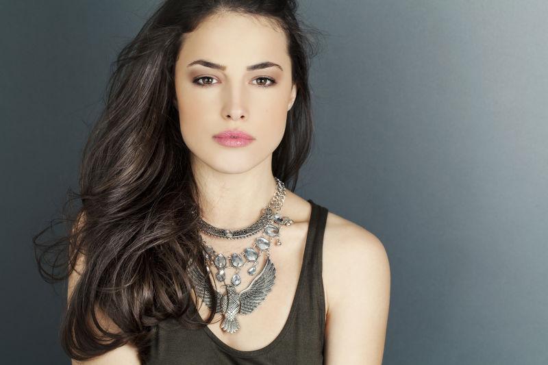 灰色背景下的戴着鹰形状银色项链的棕色长发美女