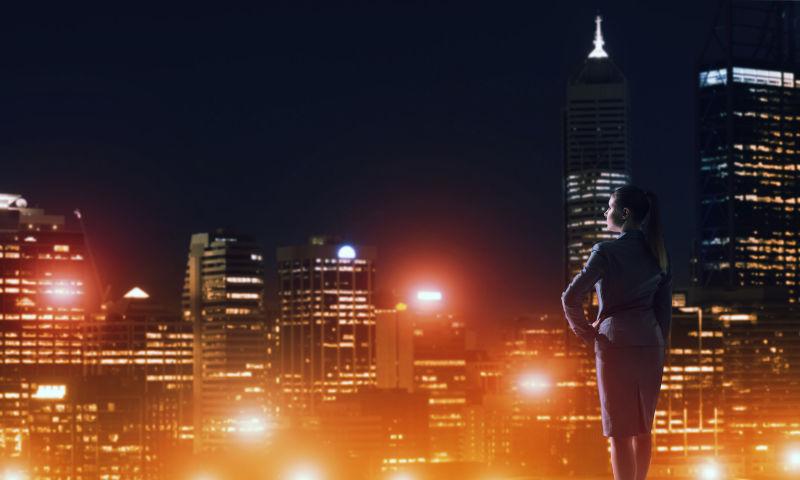穿着黑色职业服的女人看着美丽的城市夜景