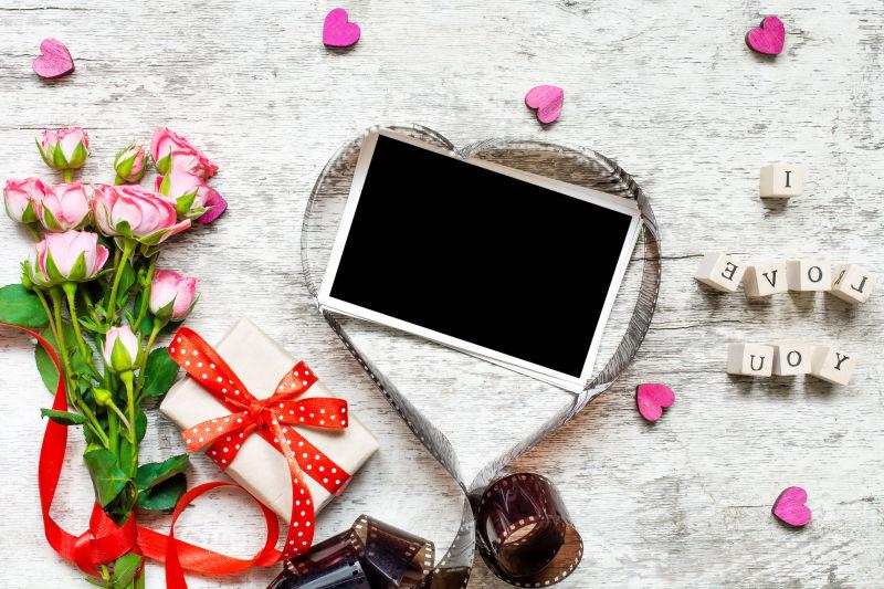 白色桌上的心形胶卷里的黑色相片和玫瑰花