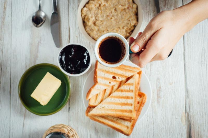 坐在木桌上吃咖啡和烤面包的男士