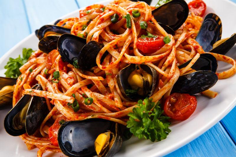 蓝色桌上的白色盘子里的贻贝和西红柿意大利面
