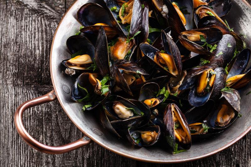 棕色木纹理桌上的铜盘里的熟贻贝