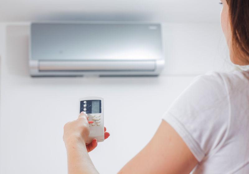 穿着白色T恤的女人用遥控操控空调