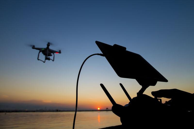 夕阳下男人在岸边操控着空中的无人机