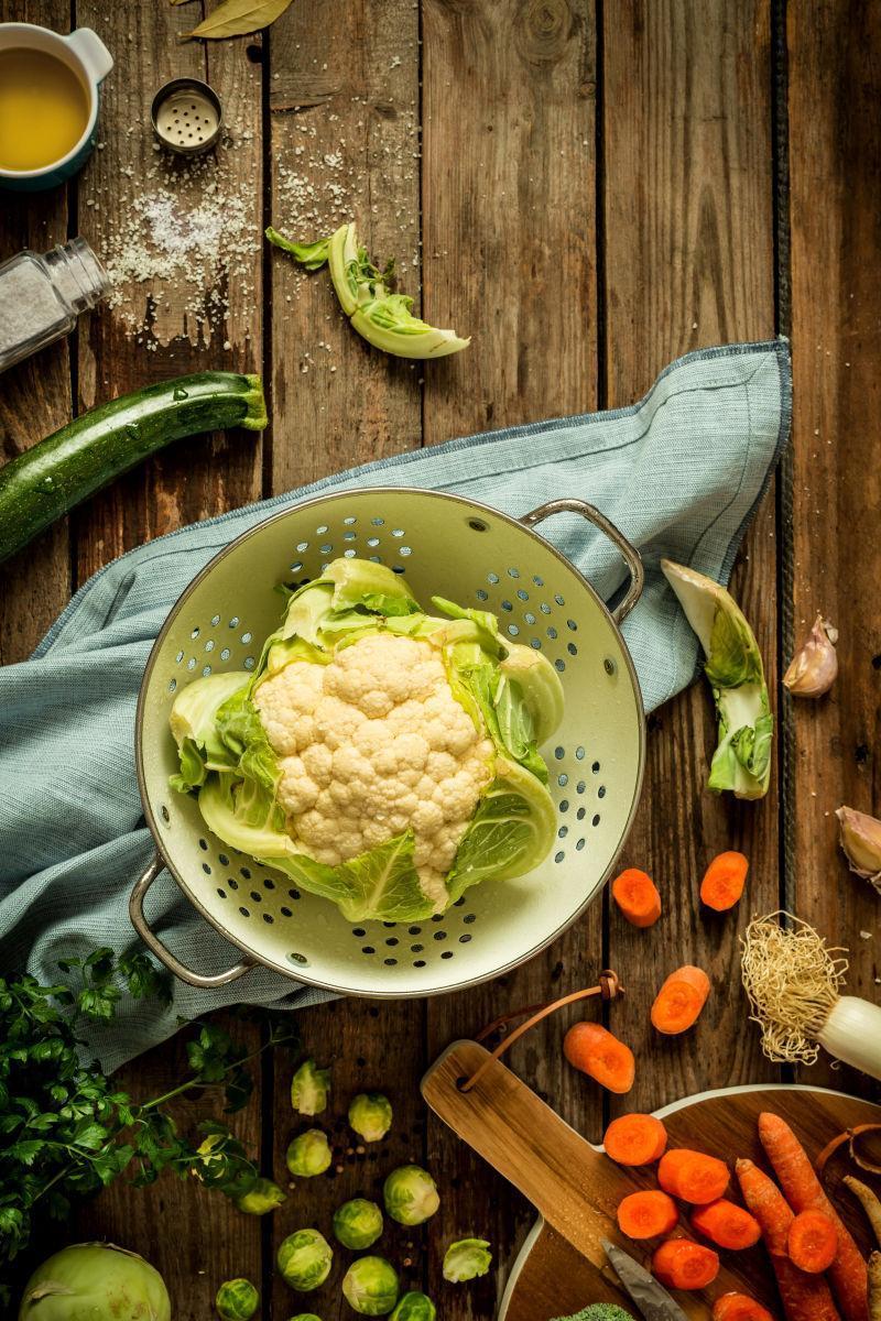 在古朴的乡村木质背景下的新鲜湿的菜花在滤器与其他蔬菜周围