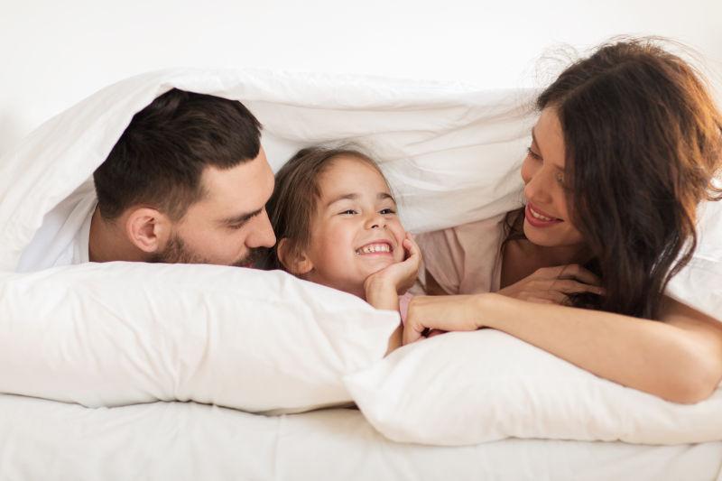 开心的钻在白色被子里的一家三口