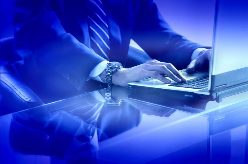 蓝色调下穿着正装使用笔记本电脑的商人