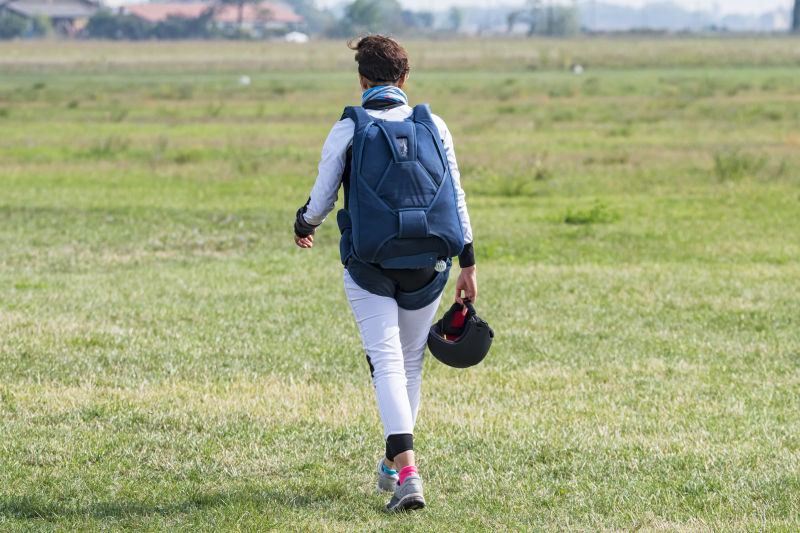 背着滑翔伞的女子走在草坪上