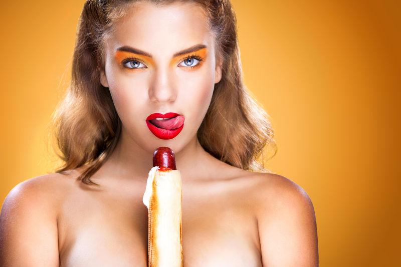 拥有完美妆容的年轻女人在大啤酒节吃大法国热狗