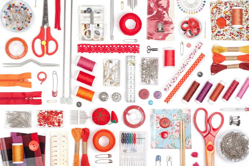 白色桌上摆放整齐的红色的缝纫工具
