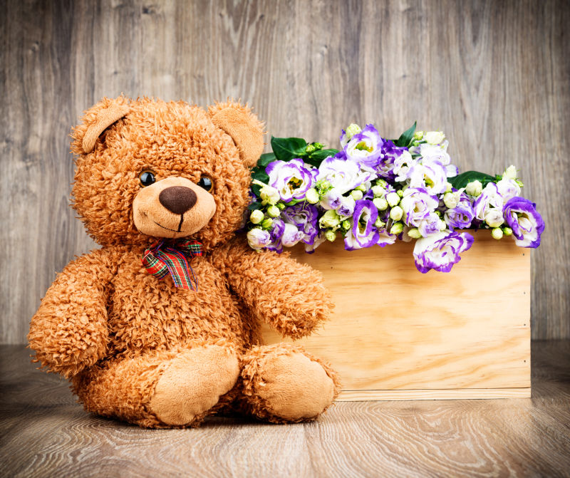 木制背景下的一束鲜花和一只泰迪熊