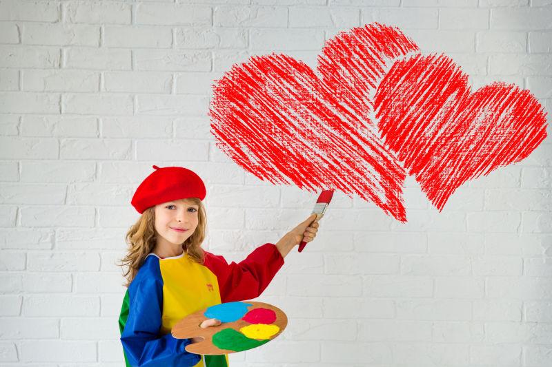 在白色墙壁上绘画爱心的快乐小女孩