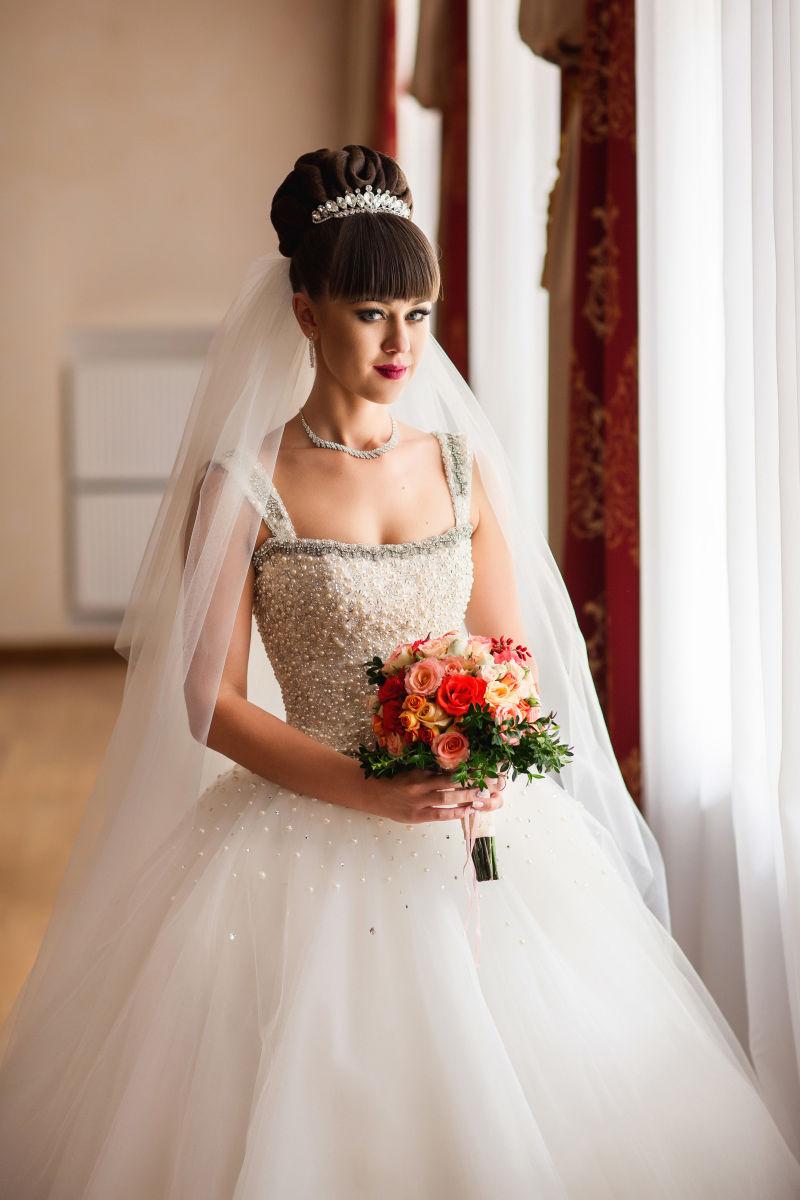 站在窗边捧着手捧花的装扮好的新娘