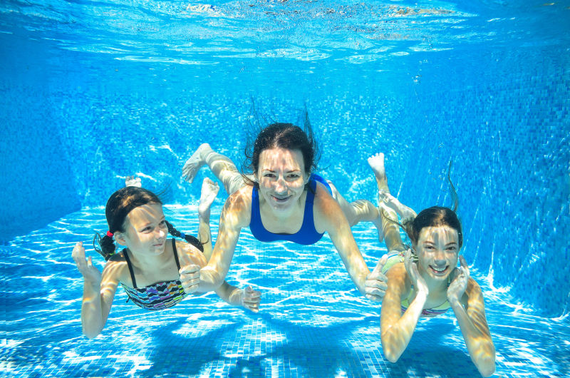 在游泳池里开心潜水游泳的妈妈和两个女儿