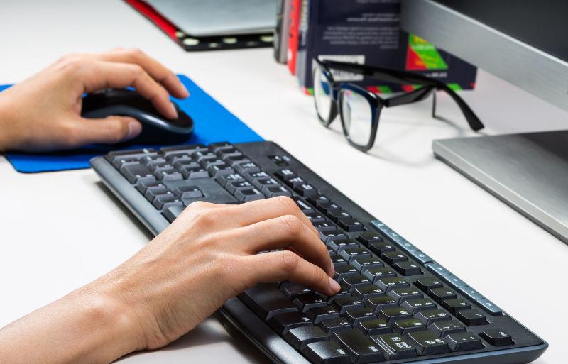 白色办公桌上使用黑色键盘和鼠标工作的一双手
