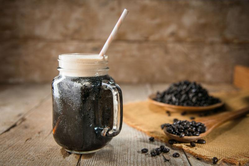 乡村木桌背景中的玻璃杯里的咖啡与咖啡豆