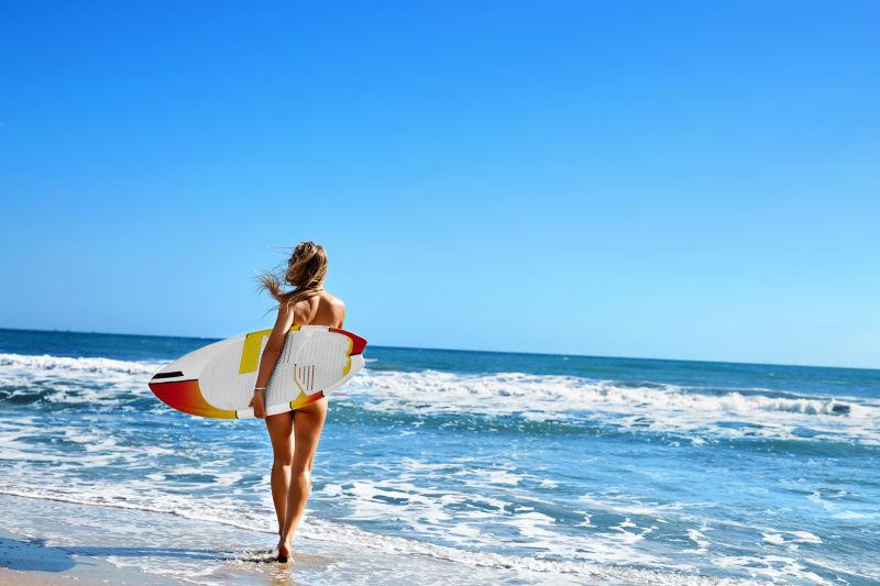 蓝色海边拿着冲浪板的美女