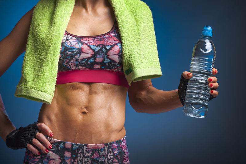 蓝色背景上拿着一瓶水的健身女人