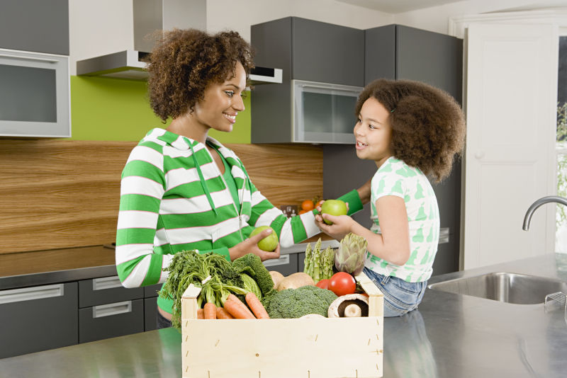 厨房里母女前面桌面上的一箱绿色蔬菜