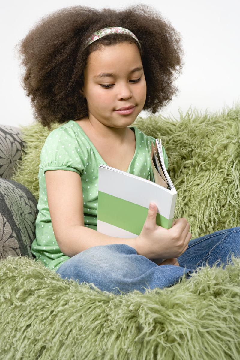 拿着书本的女孩坐在绿色的沙发上