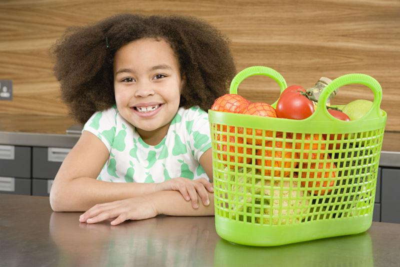 小女孩旁边有个放满了绿色蔬菜食材的购物篮