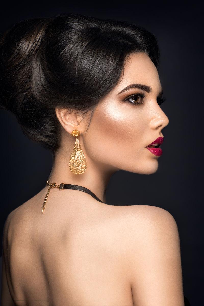 黑色背景下带着黄金珠宝的女人