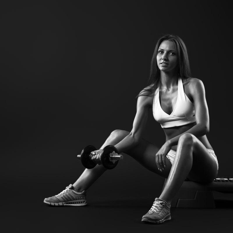 黑色背景上坐着用哑铃锻炼的健身女人