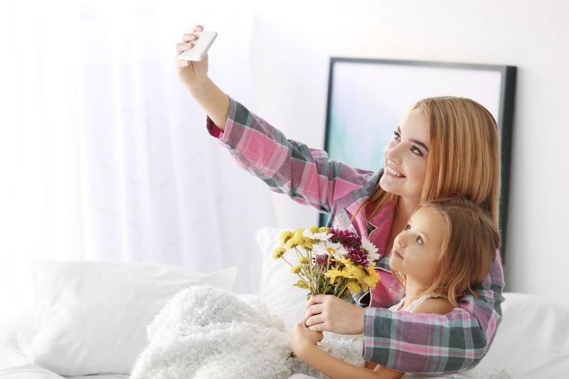 床上妈妈拿着花束和女儿在自拍