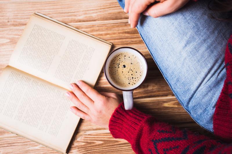 坐在木板上喝着咖啡看书的人