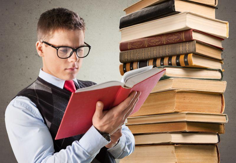 在一摞书旁边拿着红色书阅读的年轻人