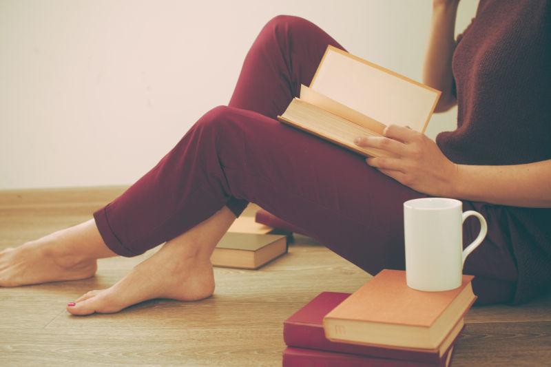 坐在木地板上穿着红色衣服看书的美女